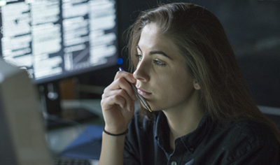 Female student in dark room examining desktop computer screen with pen in her hand